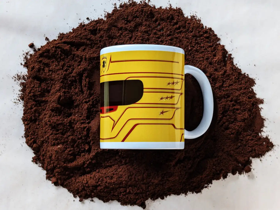 Lewis Hamilton Ferrari 2025 F1 helmet mug resting on a bed of ground coffee, showcasing the bold yellow design with red accents.