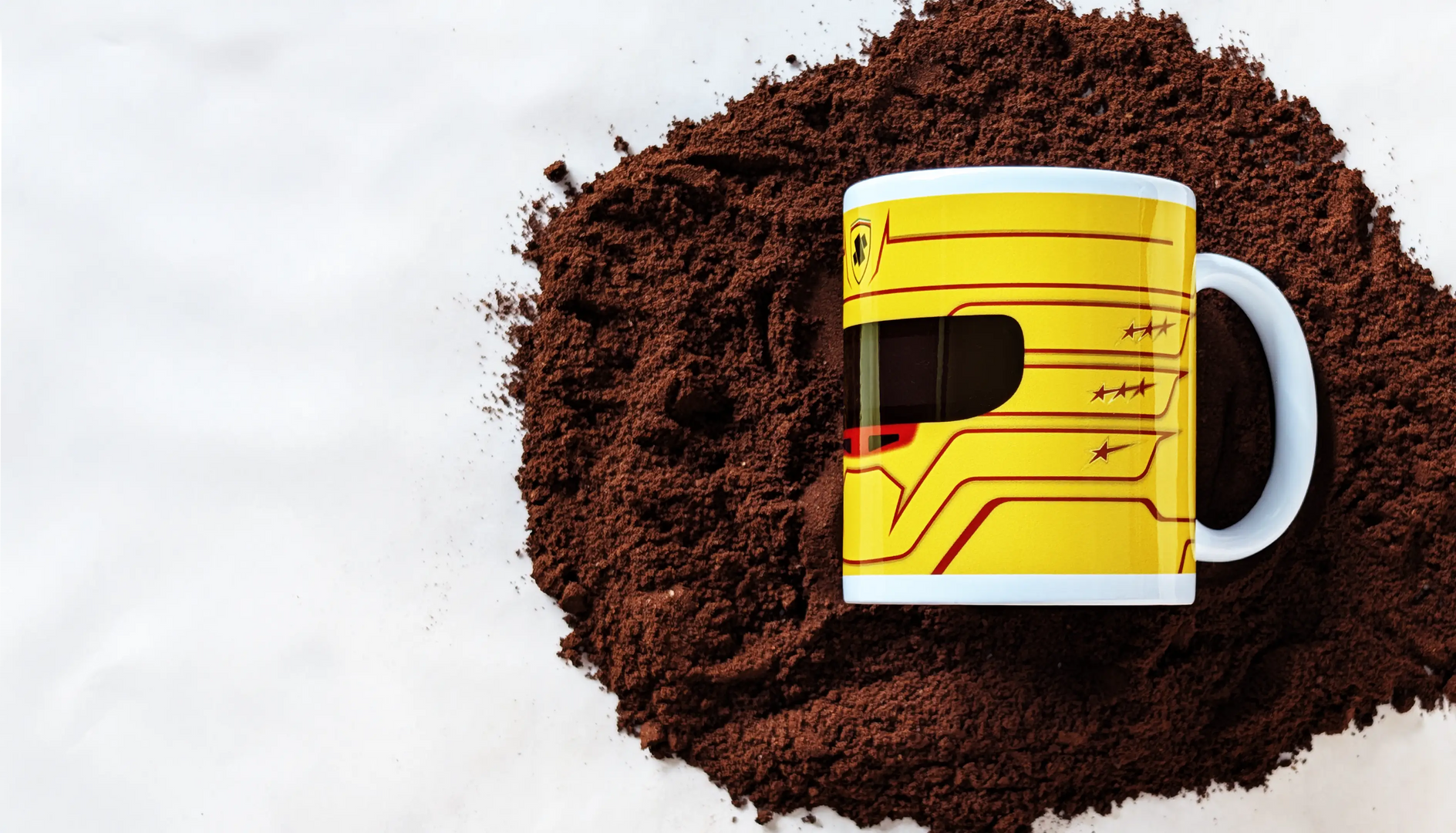 Lewis Hamilton Ferrari 2025 F1 helmet mug resting on a bed of ground coffee, showcasing the bold yellow design with red accents.